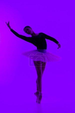 Photo for Beautiful ballerina on purple background dancing ballet. Woman performs smooth movements. Sensual dancer in tutu dress on scene under neon light. High quality photo - Royalty Free Image