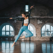 Young woman jumping in casual style - jeans and leather jacket doing ballet in old studio. Attractive ballerina practices in choreography alone. High quality photo Sweatshirt #632465962