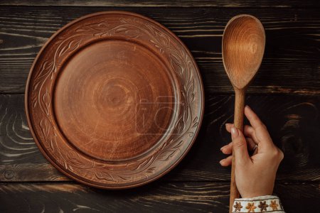 Ukrainian woman sitting in national restaurant and waiting for order. Wooden table, waiting for dish. Empty clay plate with spoon. High quality photo
