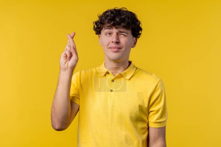 Photo for Young man praying with crossed fingers on yellow background. Guy begs someone satisfy desires, help with, prays for luck in exam. High quality photo - Royalty Free Image