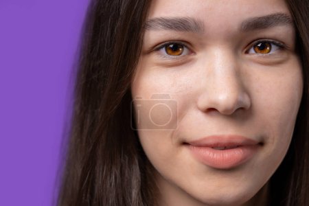 Téléchargez les photos : Close face of young pretty teenager, natural beaut. Beautiful woman with asian appearance looking at camera, violet studio background. High quality photo - en image libre de droit