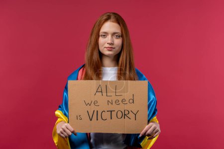 Foto de Ukrainian red-haired woman with cardboard All we need is victory on pink background. Ukraine win war. Democracy, liberty, demonstration, russian aggresion concept. High quality photo - Imagen libre de derechos