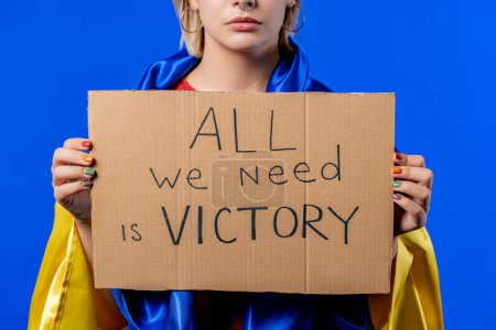 Foto de Hands of ukrainian woman with cardboard All we need is victory on blue background. Ukraine win war. Democracy, liberty, demonstration, russian aggresion concept. High quality photo - Imagen libre de derechos