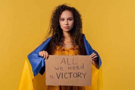 Foto de Ukrainian curly haired woman with cardboard All we need is victory on yellow background. Ukraine win war. Democracy, liberty, demonstration, russian aggresion concept. High quality photo - Imagen libre de derechos
