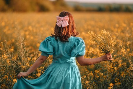 Photo for Portrait of attractive woman posing in blooming canola flowers field. Elegant girl in retro dress with bouquet, countryside nature place. Rapeseed meadow, vintage outfit, spring season - Royalty Free Image