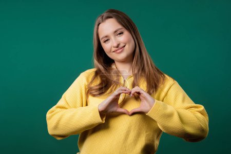 Smiling pretty woman showing sign of shape heart. Positive lady on green background. Women health, volunteering, charity donation, gratitude symbol, flirting concept. High quality 