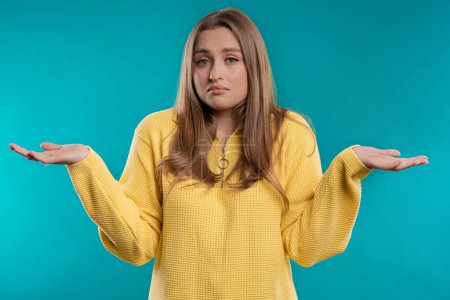 Photo for Confused pretty woman, shoulders up - can't help, makes gesture of I dont know. Difficult question, guilty reaction, puzzled stylish woman on blue background. High quality - Royalty Free Image