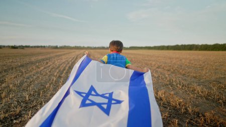 Téléchargez les photos : Joyeux petit garçon juif israélien qui court avec le drapeau national d'Israël. Jour de l'indépendance. Patriotisme. Photo de haute qualité - en image libre de droit