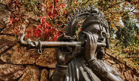 Téléchargez les photos : Statue en bronze du Seigneur Krishna jouant de la flûte. Nature automnale. Religion hindoue. Photo de haute qualité - en image libre de droit