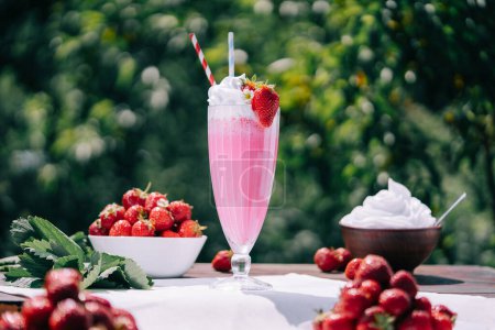 Stillleben - cremiger Erdbeer-Milchshake-Cocktail oder Smoothie mit Stroh vor Naturkulisse. Appetitlich sommerliches Dessert. Gesundes Beerenessen. Hohe Qualität 