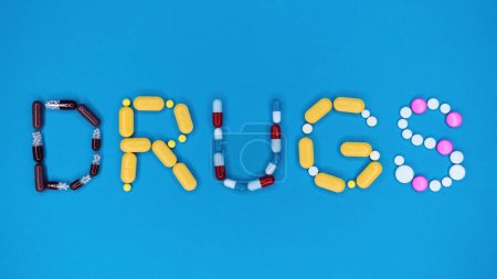 Multicolored capsules in word drugs. Blue background. Pharmacy, antidepressants, medicine concept. High quality photo