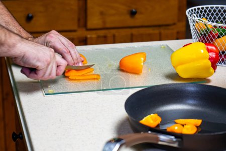 Foto de Hombre rebanando pimientos naranja en la encimera. - Imagen libre de derechos