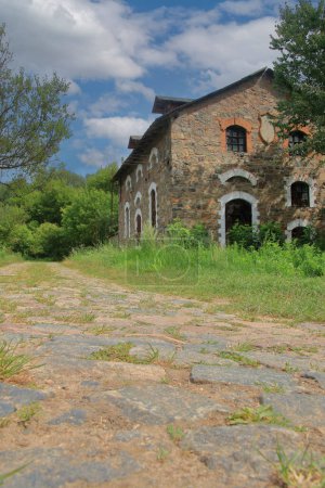The photo was taken in Ukraine. The photo shows an old stone barn on the side of a cobbled rural road.