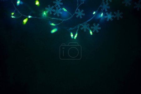 Foto de Guirnalda de árbol de Navidad verde brillante sobre fondo oscuro. Copos de nieve Confetti Decoración. Foto con espacio de copia. Fondo de vacaciones de Navidad - Imagen libre de derechos