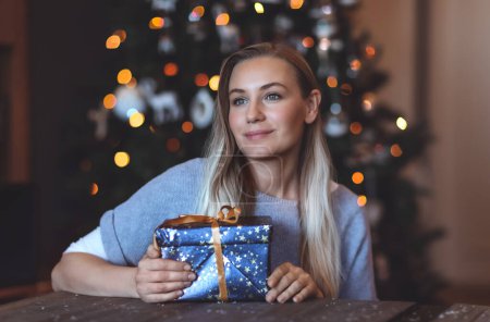 Foto de Retrato de una mujer bonita con caja de regalo festiva en casa sobre el fondo decorado del árbol de Navidad Bokeh. Felices fiestas de invierno. - Imagen libre de derechos