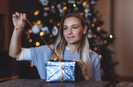 Foto de Retrato de una linda chica abriendo una caja de regalo festiva en casa sobre el fondo decorado del árbol de Navidad. Felices fiestas de invierno. Disfrutando de la celebración. - Imagen libre de derechos