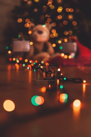 Foto de Foto temática de Navidad desenfocada. Oso con regalos bajo el resplandeciente árbol de Navidad. Luces Bokeh. Feliz Año Nuevo. - Imagen libre de derechos