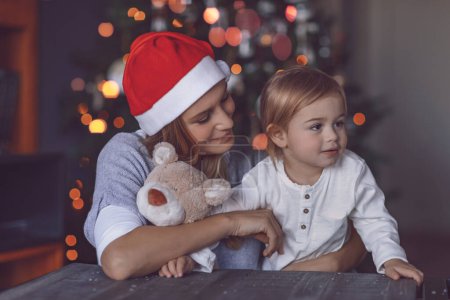 Foto de Mamá feliz con su bebé celebrando la Navidad en casa. Recibir regalos. Decoración del árbol de Navidad. Disfrutando de vacaciones de invierno en familia. - Imagen libre de derechos