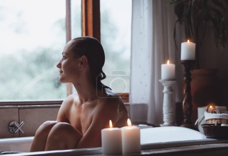 Photo for Peaceful Female Enjoying Day at Spa Hotel. Young Girl Taling Bath Candles and Looking at the Window in Bathroom. Pleasure Time. - Royalty Free Image