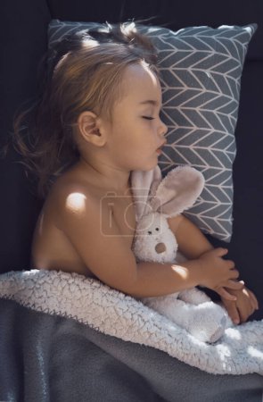 Téléchargez les photos : Beautiful child is asleep in the babys room. Portrait of a healthy pretty kid enjoying sweet dreams with his favorite soft toy rabbit. - en image libre de droit