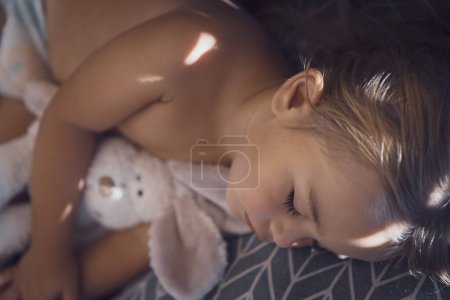 Foto de Closeup portrait of a healthy pretty kid enjoying sweet dreams with his favorite soft toy bunny. Beautiful child is asleep in the babys room. - Imagen libre de derechos