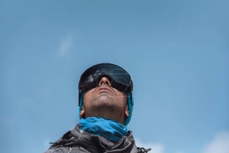Photo for Portrait of a Handsome Man Dressing Ski Goggles Looking Up in the Sky over Blue Clear Sky Background. Active Lifestyle. Happy Vacation. - Royalty Free Image