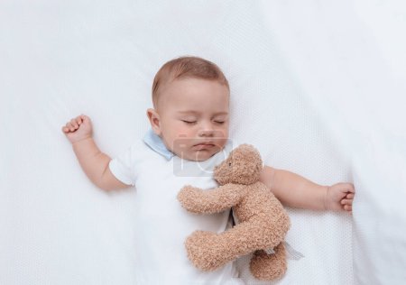 Téléchargez les photos : Portrait d'un gentil petit garçon dormant dans son berceau avec son meilleur ami ours en peluche. Bonne enfance en bonne santé. - en image libre de droit