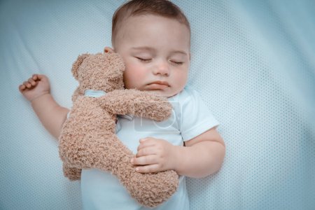 Foto de primer plano de un pequeño bebé lindo durmiendo en casa en la cuna con un oso de juguete suave. Dulce niña durmiendo. Vida familiar feliz y saludable.