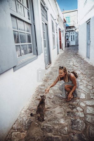 Foto de Irl turista caminando por las lindas calles blancas y estrechas de Grecia. Mascotas al gato. Disfrutando de unas felices vacaciones activas en Europa. - Imagen libre de derechos