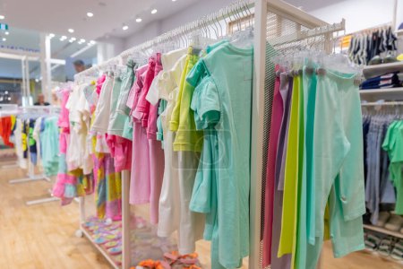 Téléchargez les photos : Beaux vêtements colorés pour enfants lumineux sur cintres dans le magasin. Du shopping pour une jeune mère. Nouvelle collection d'été. - en image libre de droit