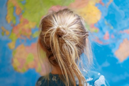 Photo for Closeup photo of a rear view on a little child carefully considers world map. Cute kid on a geography lesson. Dreaming about travel. - Royalty Free Image