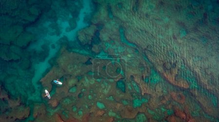 Téléchargez les photos : Fond marin aérien. Incroyable belle photo d'une eau transparente en Méditerranée. Vue par drone sur deux personnes montant un soup dans l'eau claire et calme. Personnes actives en été. - en image libre de droit