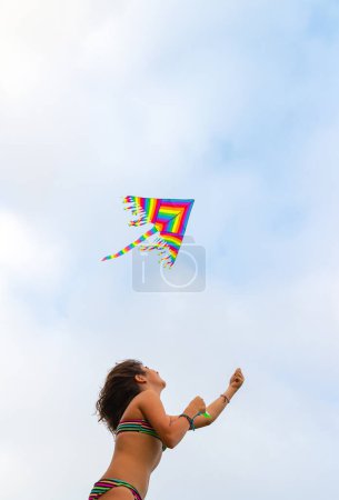 Foto de Chica alegre vuela una cometa en la playa. Disfrutando de juegos activos al aire libre. Actividades en la playa. Felices vacaciones de verano. - Imagen libre de derechos