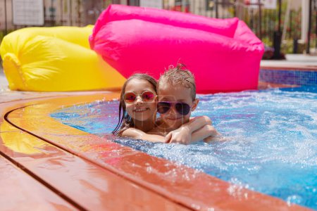 Foto de Dos niños alegres disfrutando de agua refrescante fresca en la piscina. Feliz fin de semana en Aquapark. Disfrutando de las vacaciones de verano en el resort de playa. - Imagen libre de derechos