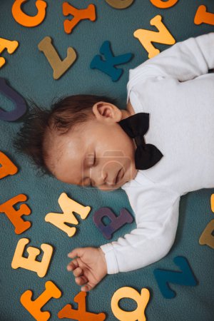 Photo for Closeup portrait of a pretty serious baby boy sleeping at home in childs bedroom among colorful ABC letters. Back to school concept. - Royalty Free Image