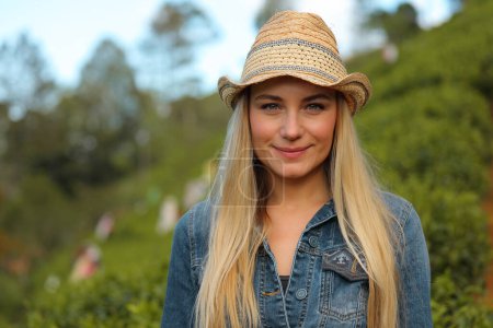 Téléchargez les photos : Portrait d'une belle fille blonde portant un chapeau de paille élégant parmi la verdure sur la station tropicale. Bénéficiant d'une nature exotique fraîche incroyable. - en image libre de droit