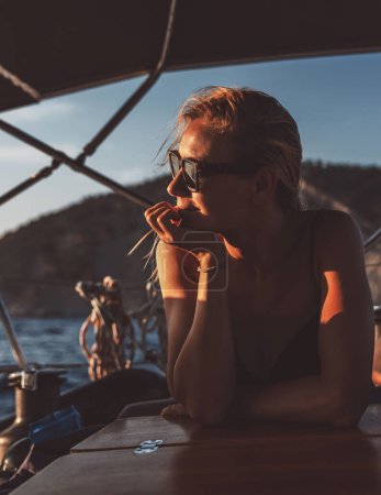 Téléchargez les photos : Portrait d'une belle jeune femme jouissant d'un coucher de soleil chaud incroyable sur voilier. Vue magnifique sur la mer parmi les hautes montagnes. - en image libre de droit