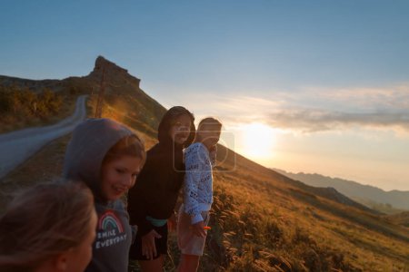 Téléchargez les photos : Quatre amis heureux avec plaisir passer du temps ensemble à l'extérieur. Bénéficiant d'une belle vue sur une haute montagne majestueuse dans la lumière douce du coucher du soleil. Bonne vie de bébé. - en image libre de droit