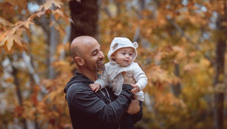 Téléchargez les photos : Portrait d'un jeune père joyeux avec son mignon petit fils à la main sur un fond de feuillage d'automne doré. Journée en famille dans la forêt d'automne. - en image libre de droit
