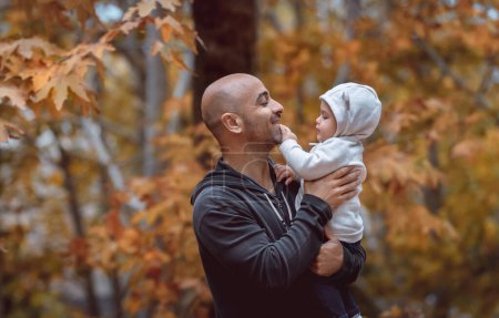 Foto de Retrato de un joven padre alegre con su pequeño y lindo hijo sobre un fondo dorado de hojas de otoño. Día familiar en el parque de otoño. - Imagen libre de derechos