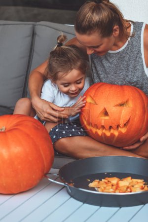Téléchargez les photos : La photo montre une famille heureuse. Maman tient dans ses mains une citrouille effrayante qu'elle et son fils sculptés de leurs propres mains pour célébrer Halloween. - en image libre de droit