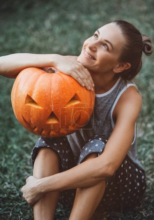 Téléchargez les photos : La photo montre une fille heureuse qui aime célébrer Halloween. Tenir une citrouille effrayante dans ses mains. Jack o lanterne avec un visage maléfique. - en image libre de droit