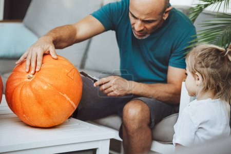 Photo for Young father with his little son making homemade jack-o-lantern for Halloween holiday. Carving scary face on the pumpkin. Happy family tradition. Autumn season. - Royalty Free Image