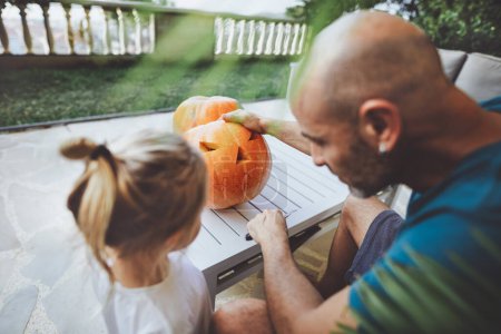 Photo for Happy young family together making decorations for Halloween holiday. Home party decor. Father with his little son carving face on the pumpkin. Nice traditional fun in autumn season. - Royalty Free Image