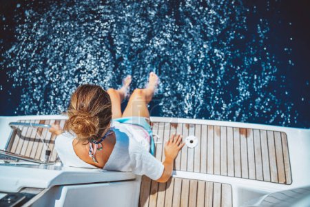 Téléchargez les photos : Belle femelle assise sur le pont du voilier et profitant de l'eau de mer. Passer des vacances d'été sur la plage. Mode de vie sain et heureux. - en image libre de droit