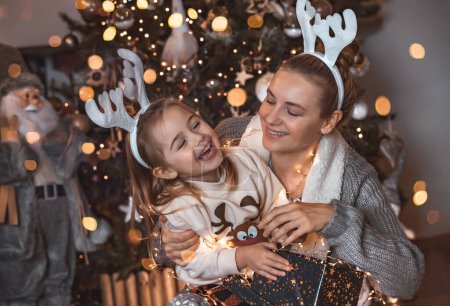Foto de Retrato de una feliz familia feliz jugando cerca del árbol de Navidad en casa. Llevando bonitos cuernos festivos de Rudolph. Disfrutando de la víspera de Navidad. - Imagen libre de derechos