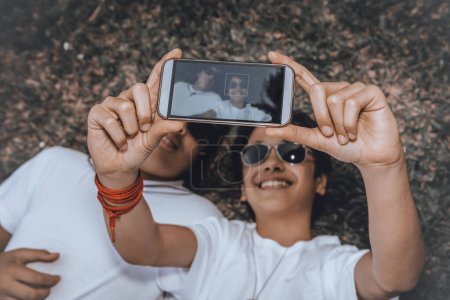 Photo for Two young people take a creative photo in a horizontal position, lying on the ground. Dark glasses protect them from the scorching sun. - Royalty Free Image