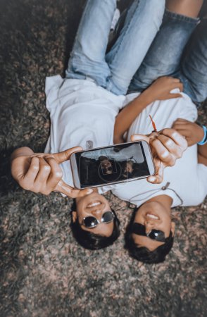 Photo for Two young people take a creative photo in a horizontal mode, lying on the ground. Dark glasses protect them from the scorching sun. - Royalty Free Image