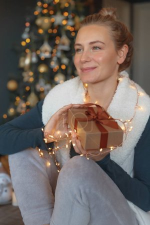 Foto de Retrato de una mujer bonita que recibe una caja de regalo para Navidad. Happy Girl recibió un regalo para las vacaciones de invierno. Celebrando Navidad y Año Nuevo en casa. - Imagen libre de derechos