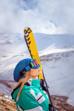 Photo for Profile portrait of an active girl enjoying beautiful winter ski resort. Pretty woman wears protective helmet and mask. Standing on the top of mountain - Royalty Free Image